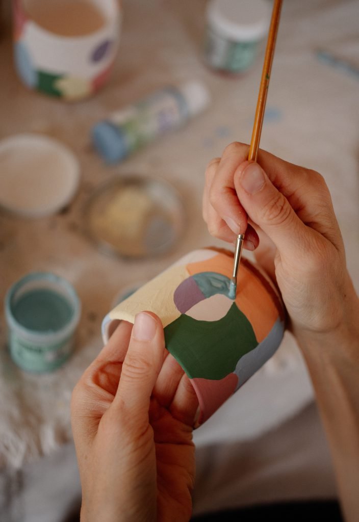 Deux mains peignent des motifs géométriques sur une tasse